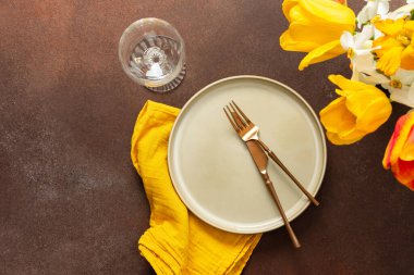A beautifully arranged spring table setting features a light plate, gold-tone utensils, and vibrant flowers. The yellow napkin adds a pop of color, creating a joyful atmosphere for dining