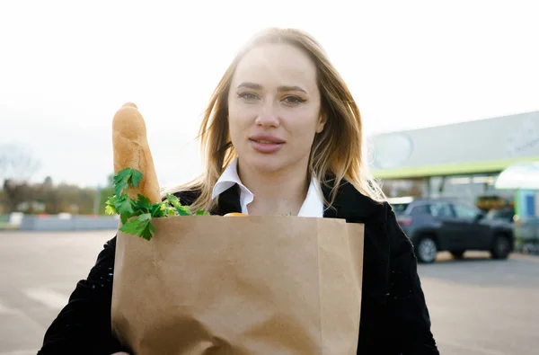 Zengin yeşilliklerle çevrili, açık havada çekilmiş bir portre. Elinde süpermarketten taze ve sağlıklı ürünlerle dolu bir kesekağıdı var. Sağlıklı bir alışverişin özünü yakalıyor.