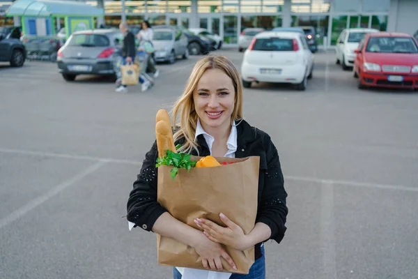 Güneşli bir günde, elinde kağıt torbalarla süpermarketin dışında taze ve sağlıklı yiyecekler taşıyan parlak gülüşlü kadınlar..