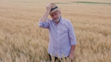 Gün batımında ekilmiş bir buğday tarlasında duran kovboy şapkalı memnun bir işadamının büyüleyici görüntüsü iş zekasının ve iş zekasının başarılı bir kombinasyonunu sembolize ediyor.