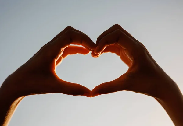 Dişi eller kalp şeklinde gökyüzüne karşı güneş ışınlarını uzatıyorlar. Sevgi dolu kalp şeklinde eller. Yüksek kalite fotoğraf