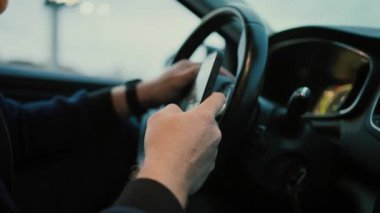 Kimliği belirsiz erkek sürücünün elinde direksiyon tutarken ve hisse senedi alırken cep telefonunun ekranına bakmasından. 