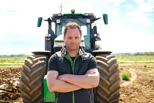 Yetenekli bir çiftçi, saban traktörünün yanında gururla durur ve arazi yönetimi ve toprak hazırlama konusundaki uzmanlığını gösterir..
