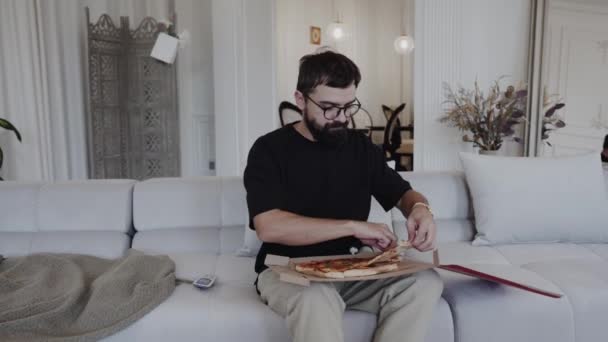 一个男人躺在房子里舒适的沙发上 享受披萨 一株家居植物坐在窗边 给房间增添了温暖 — 图库视频影像