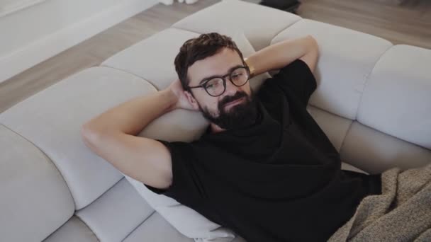 Homem Com Barba Óculos Está Reclinado Num Sofá Mãos Atrás — Vídeo de Stock