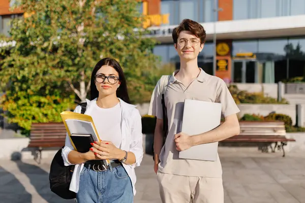 Bir erkek ve bir kız büyük bir binanın önünde yan yana dururlar, ikisi de gözlük takar ve gülümserler. Bir ağaç ve bir bitki Toplumun cazibesini arttırır