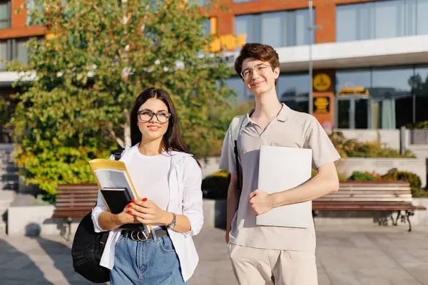 Bir adam ve bir kadın binanın önünde yan yana duruyorlar, gülümsüyorlar ve karşılıklı jestler yapıyorlar. Bir ağaç ve bitki, bir sonraki seyahatlerini planlarken boş sahneyi süsler.