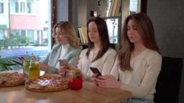 Kadın arkadaşlar, kafeteryada öğle yemeği yerken pizza yiyip kavanoz dolusu kokteyl içerek cep telefonlarını karıştırıyorlar. 