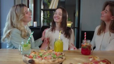 Günlük kıyafetlerle mutlu genç kadınlar ahşap masada lezzetli pizzalarla oturuyor ve restoranda eğlenirken gülüyorlar. 