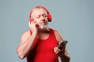 Yaşı ilerlemiş bir adam teknolojiden faydalanıyor. Stüdyo onun mavi arka planında bir uygulama kullanarak kulaklıkla müzik dinliyor. yeni aygıtlara adapte olan yaşlılar.