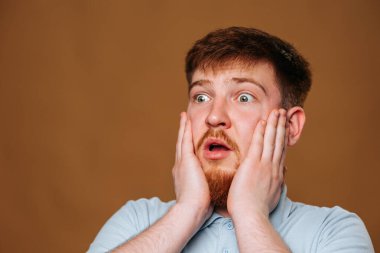 The teenage guy looks surprised and amazed as he strikes a pose in front of the camera in a studio. This adolescent male looks puzzled and shocked as he gazes into the camera lens during