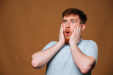 This young redhead guy looks shocked and amazed while posing for the camera in a studio. The teenager seems puzzled and surprised as he looks directly into the camera in a studio setting.