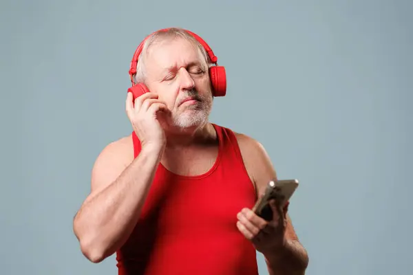 Yaşı ilerlemiş bir adam teknolojiden faydalanıyor. Stüdyo onun mavi arka planında bir uygulama kullanarak kulaklıkla müzik dinliyor. yeni aygıtlara adapte olan yaşlılar.