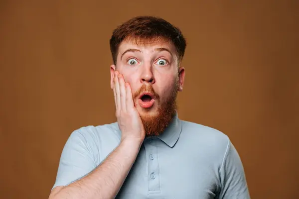 Adam, şaşırmış görünüyor, elini yanağına tutuyor, sakalının yanında. Jestte gömleğinin kolları ve yakası görünüyor.