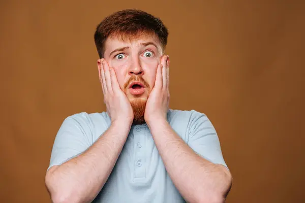 The teenage guy looks surprised and amazed as he strikes a pose in front of the camera in a studio. This adolescent male looks puzzled and shocked as he gazes into the camera lens during