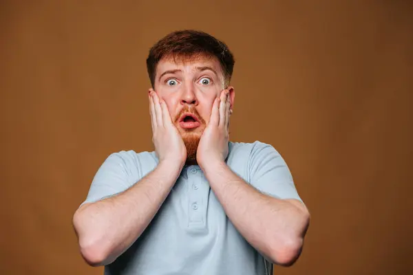 The teenage guy looks surprised and amazed as he strikes a pose in front of the camera in a studio. This adolescent male looks puzzled and shocked as he gazes into the camera lens during