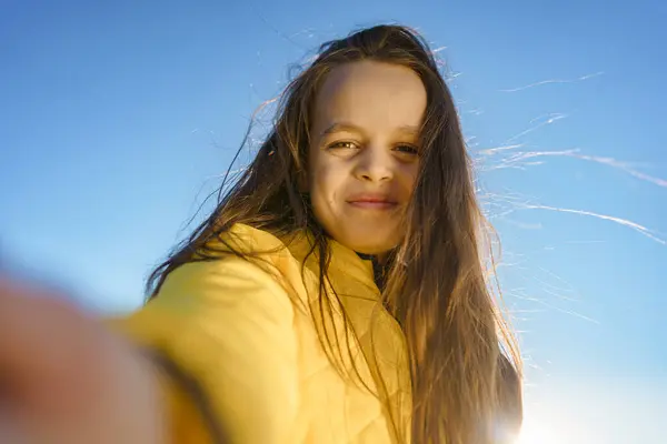 Sarı bir ceketle gülümseyen neşeli bir kız, açık mavi bir arka planı var. Yakından ve parlak bir şekilde yakalandı..