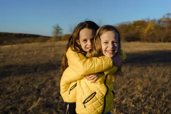 Sarı ceketli neşeli ikiz kardeşler güneşli bir sonbahar tarlasında birbirlerine sarılıp kardeş bağlarını ifade ediyorlar..