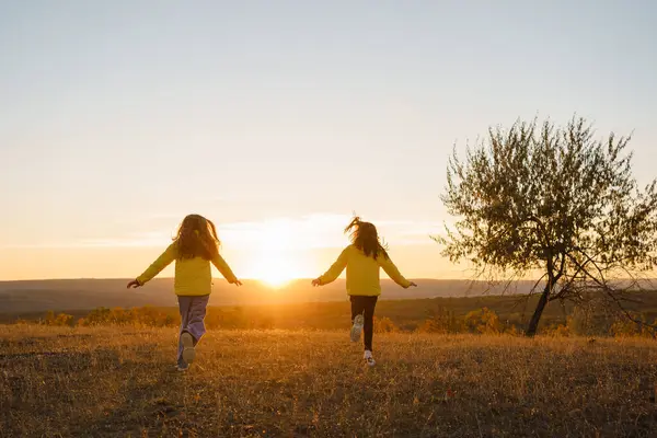 Gün batımında bir tarlada neşeyle oynayan iki çocuk doğanın güzelliğini kucaklıyor ve tasasız hissediyorlar.