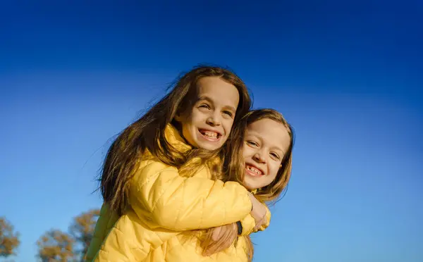 Sarı ceketli iki neşeli kardeş güneşli bir günde dışarıda eğleniyor, kahkahalarını ve mutluluklarını paylaşıyorlar.