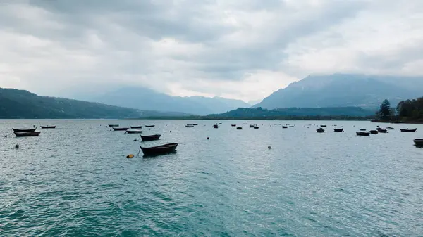 Tepelerin ortasındaki teknelerle sakin bir göl ve bulutlu bir gökyüzü dinlenmek ve doğanın tadını çıkarmak için sakin bir ortam sağlıyor.
