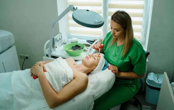 Yüz soyma maskesi, kaplıca güzellik tedavisi, cilt bakımı. Güzellik salonunda güzellik uzmanından yüz bakımı alan bir kadın. Kozmetik uzmanı yüz tedavisi yapıyor ve yüz maskesi takıyor. Yüksek kalite fotoğraf