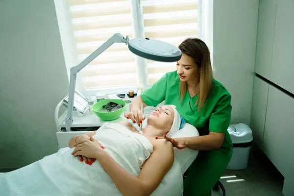 Yüz soyma maskesi, kaplıca güzellik tedavisi, cilt bakımı. Güzellik salonunda güzellik uzmanından yüz bakımı alan bir kadın. Kozmetik uzmanı yüz tedavisi yapıyor ve yüz maskesi takıyor. Yüksek kalite fotoğraf