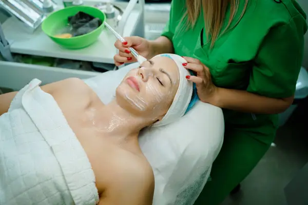 Yüz soyma maskesi, kaplıca güzellik tedavisi, cilt bakımı. Güzellik salonunda güzellik uzmanından yüz bakımı alan bir kadın. Kozmetik uzmanı yüz tedavisi yapıyor ve yüz maskesi takıyor. Yüksek kalite fotoğraf