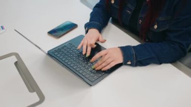 Yakın plan bir fotoğraf, modern bir çalışma alanında akıllı bir telefonun yanında aktif olarak dizüstü bilgisayarda yazan elleri gösteriyor.