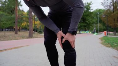 Arka planda ağaçlar, dizlerde ağrı, eklem ağrıları, dışarıda egzersiz yapmak için dizlerde ağrı şikayeti olan bir adam parkta koşarken çok acı çekiyor.