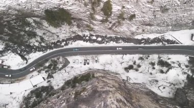 Kayalık arazi ve yemyeşil yemyeşil ile çevrili görkemli dağların arasından dolambaçlı bir yol manzarası.
