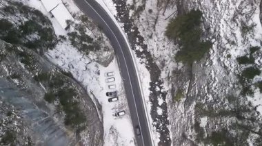 Nefes kesen bir hava manzarası, güzel karlı bir arazide park halindeki araçların yanında dönen bir yol yakalıyor.