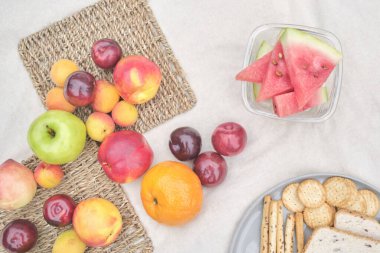 Healthy picnic breakfast: whole grain bread and crackers and variety of fresh fruits, watermelon, peaches, plums, apples. Top view.