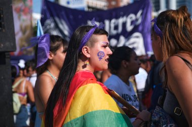 Buenos Aires, Arjantin; 8 Mart 2023: Uluslararası feminist grev. Omuzlarında gökkuşağı bayrağı olan genç bir kadın ve yanağında makyaj olarak feminist mücadelenin mor sembolü..