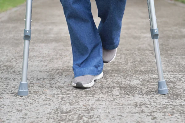 Detail of the legs and feet of an unrecognizable person walking with the help of crutches.