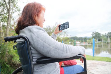 Tekerlekli sandalyedeki Latin olgun kadın dışarıdaki akıllı telefonuyla konuşurken gülümsüyor. İletişim kurmak için kullanılan teknoloji insanları mutlu eder..