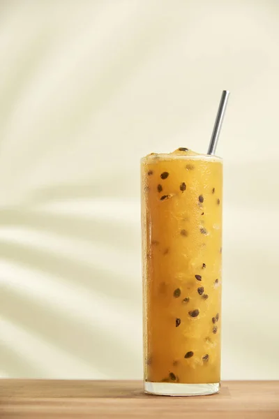 stock image Glass of a refreshing passion fruit drink, juice or cocktail, with a reusable ecological straw on a wooden surface. The shadow of a tropical leaf is projected on the back wall.