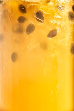 Sarı tropikal arka plan, tutkulu bir meyveye yakın taze meyve suyu, meyve suyu veya kokteyl, tohumlar havada süzülür ve yoğunlaşma bardakta düşer..