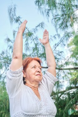 Beyaz elbiseli, kıdemli İspanyol kadın parkta yoga yapıyor. Konseptler: sağlık, aktif ve sağlıklı yaşam tarzı.