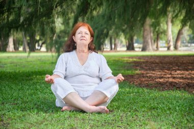 Beyaz elbiseli olgun bir Latin kadının portresi. Yoga yapıyor ve parkta meditasyon yapıyor. Konseptler: sağlık, huzur ve sağlıklı yaşam tarzı.
