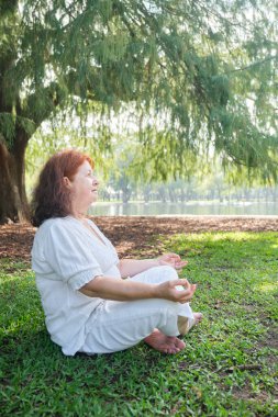 Beyaz elbiseli olgun bir Latin kadının portresi parkta yoga ve meditasyon yapıyor. Konseptler: sağlık, sükunet ve zihinsel sağlık.