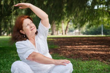 Beyaz elbiseli yaşlı bir İspanyol kadının portresi parkta yoga yapıyor. Konseptler: sağlık, canlılık, aktif ve sağlıklı yaşam tarzı.