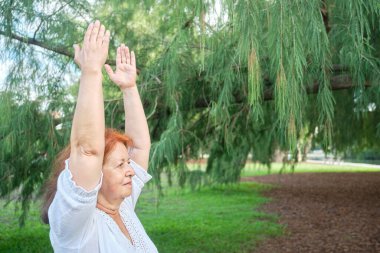 Beyaz elbiseli, kıdemli İspanyol kadın parkta yoga yapıyor. Konseptler: sağlık, aktif ve sağlıklı yaşam tarzı.