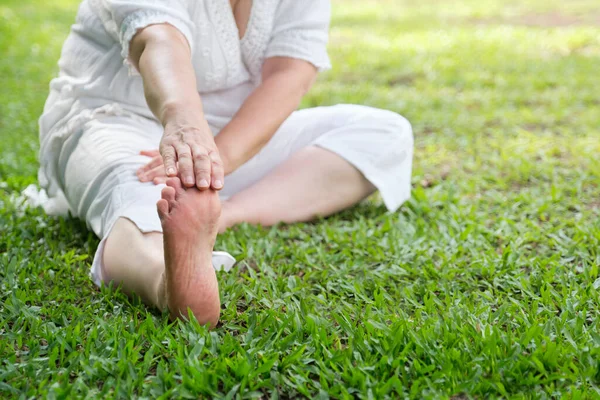 stock image Unrecognizable woman in white clothes and barefooted doing stretching exercises outdoors in a park. Concepts: wellness, vitality, active and healthy lifestyle.