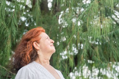 Latin, son sınıf kızıl saçlı, gülümseyen ve doğada hayal kuran bir kadının portresi. Kopya alanı ile parlak kompozisyon. Kavram: Huzur ve mutluluk emeklilik sırasındaki boş vakitlerin keyfini çıkarmak.