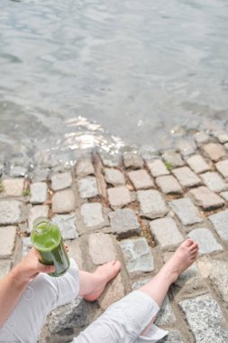 Kimliği belirsiz kişi dışarıda bir şişe yeşil meyve suyu tutuyor. Konseptler: sağlık, beslenme, sağlıklı ve sürdürülebilir yaşam tarzı.