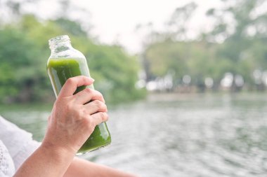 Tanınmayan biri cam şişeden yeşil meyve suyu içiyor. Konseptler: sağlık, beslenme, sağlıklı ve sürdürülebilir yaşam tarzı.