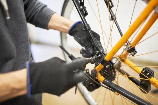 Maintenance of a bicycle: hands of an unrecognizable person using gloves disassembling an orange bike with a hex allen key in his repair shop.