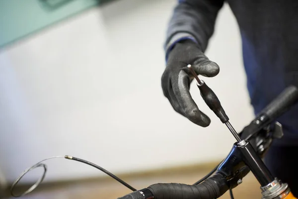 Maintenance of a bicycle: unrecognizable man using protective gloves disassembling a bike with a hex allen key in his repair shop.