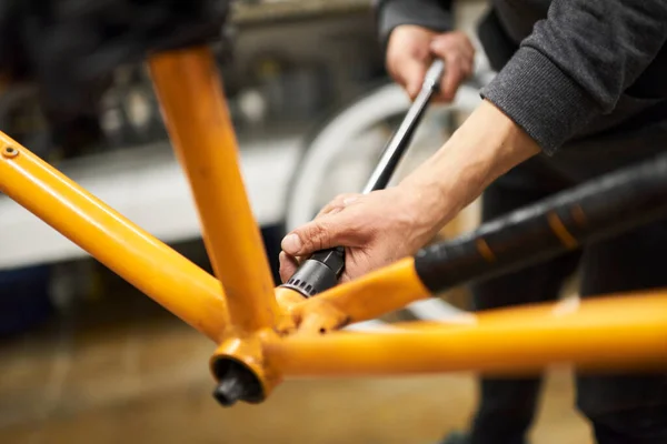 Unknown man disassembling an orange bike to paint it, change the color of the frame, at his repair shop.